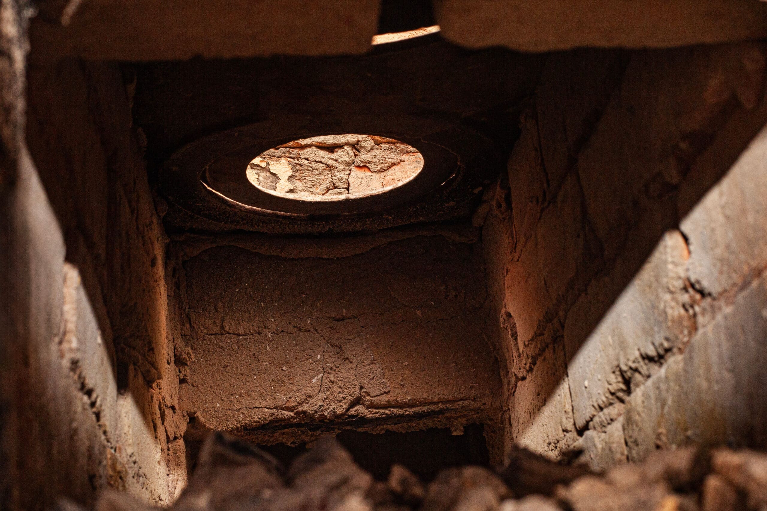 A view from inside a coal and wood stove, with ash residue and smoldering flint and soot on the chimney